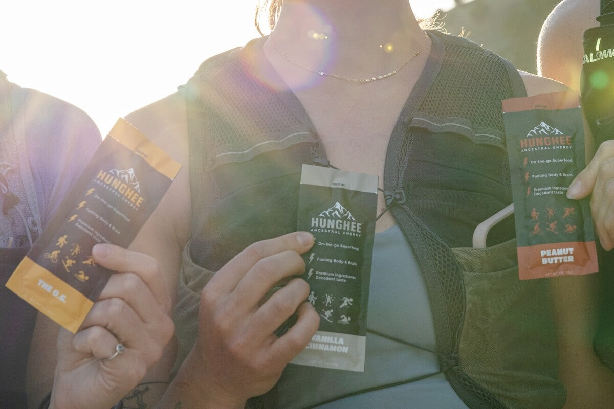 Hikers holding Hunghee Ancestral Energy packs with sunlight in the background – animal-based energy snack made from raw honey, ghee, and sea salt