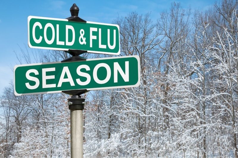 Green street sign reading Cold & Flu Season against snowy trees — ancestral winter tips