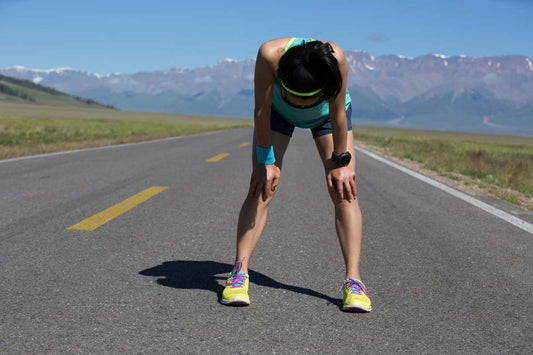 Runner bent over on an empty road with mountains after a hard workout, endurance recovery
