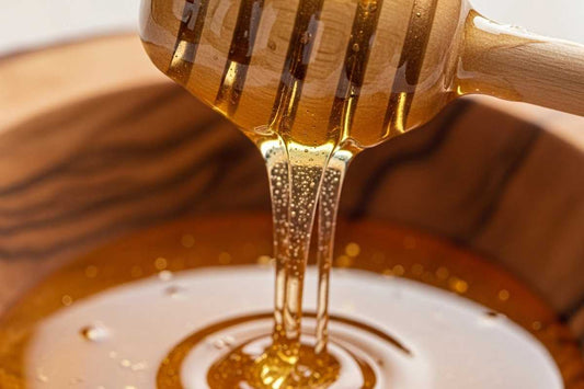 Golden raw honey flowing from a dipper into a wooden bowl, raw honey