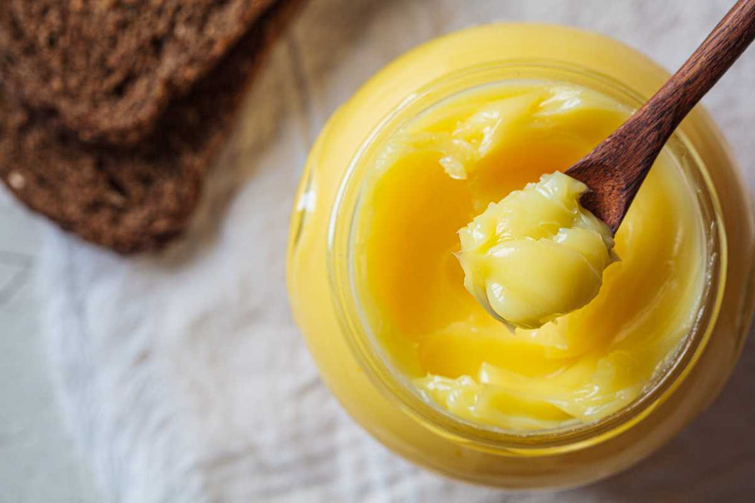 Jar of ghee with a wooden spoon on a marble counter, grass-fed ghee.