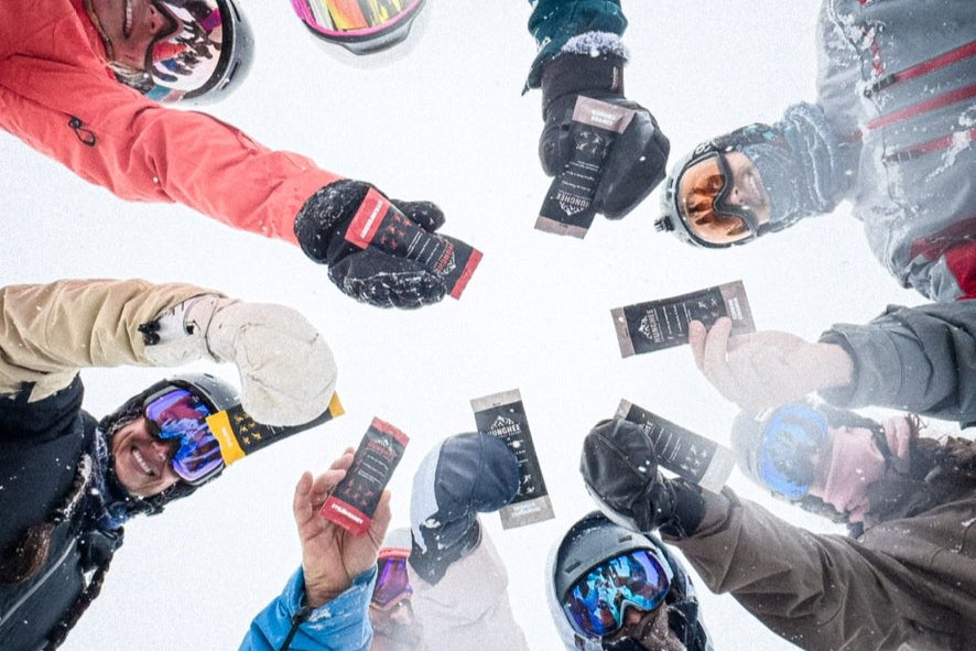 Group of winter athletes holding Hunghee Energy packs on the mountain – fueling skiers, snowboarders, and outdoor adventurers
